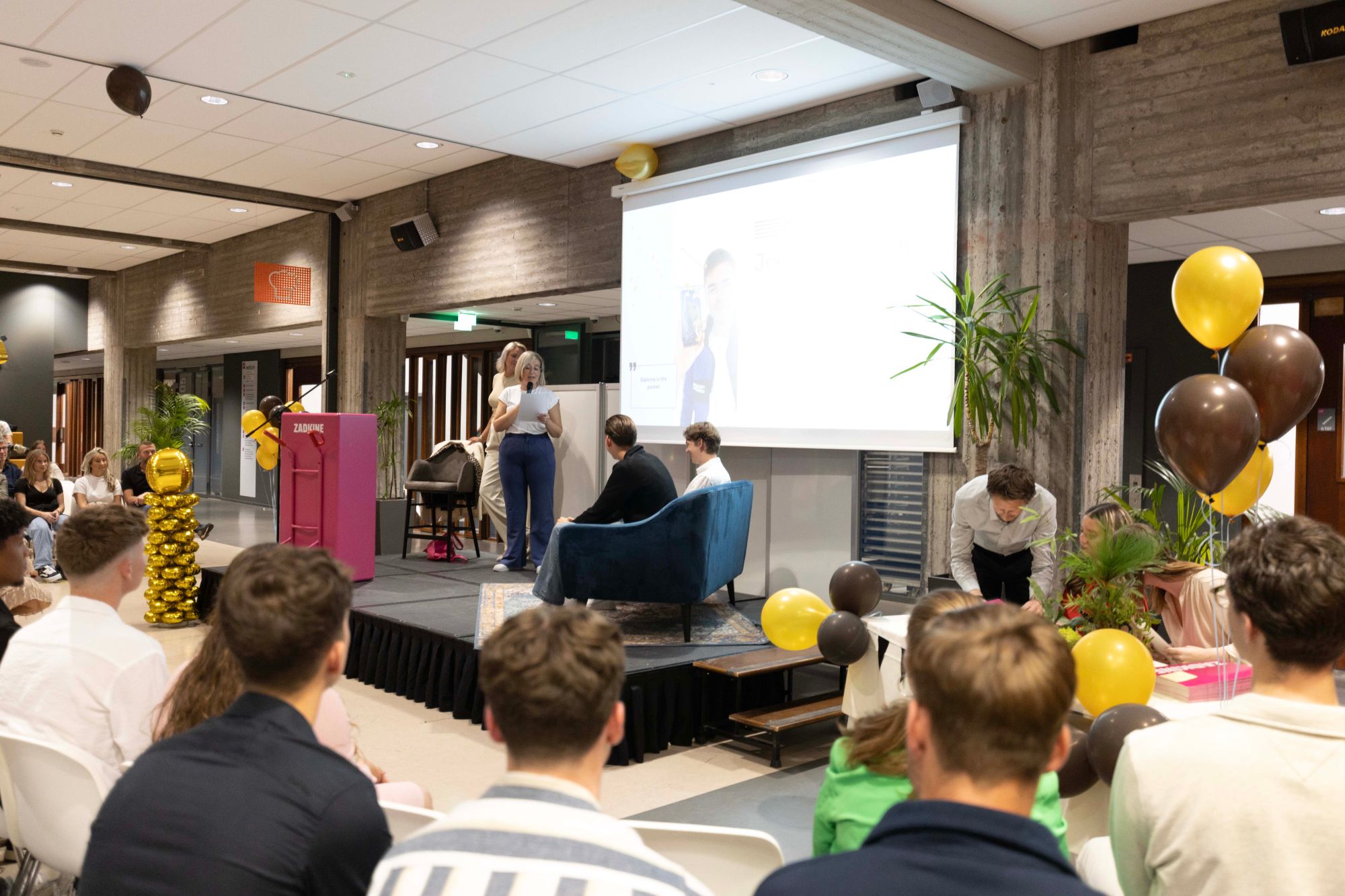 Marjolein presenteert een evenement op een podium voor een volle zaal