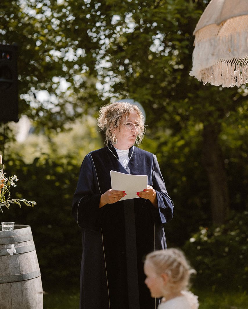 Marjolein leest de ceremonie voor, in een tuin onder een franjeparasol